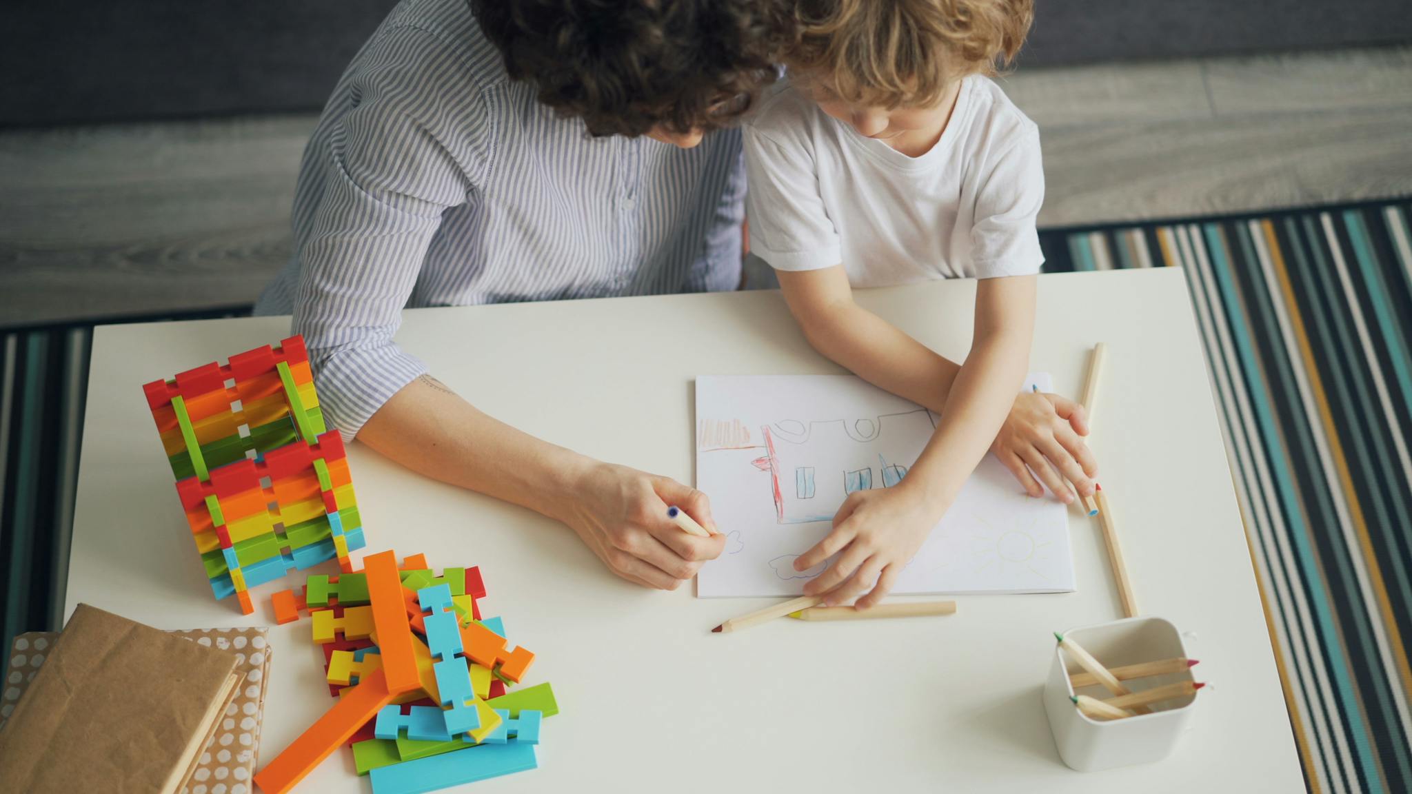 A mother and son enjoying a creative drawing session with colorful blocks at home.